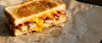 Grilled cheese sandwich with melted cheddar and crispy bacon on toasted bread, comfort food for restaurant menus and culinary marketing materials.