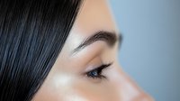 Close up profile view of Asian woman with flawless skin, long eyelashes, and sleek black hair against soft blue background, showcasing natural beauty and professional makeup artistry.