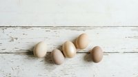 Fresh organic eggs in natural beige and brown tones arranged on rustic white wooden background for healthy cooking and farm-to-table cuisine concepts.