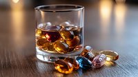 Glass of whiskey with ice cubes on dark wooden table, amber liquid with rocks, moody bar atmosphere.