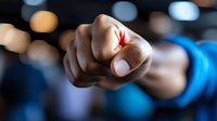 Close-up of fist with red maple leaf tattoo on knuckle, person wearing blue clothing against blurred bokeh background.