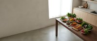 Fresh organic vegetables and fruits arranged on wooden table in modern minimalist kitchen interior with natural lighting for healthy cooking preparation.