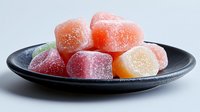 Colorful fruit gummy candies covered in sugar crystals arranged on dark ceramic plate against white background for confectionery and sweet treat designs.