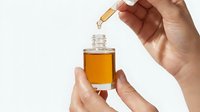 Female hands applying golden facial serum with dropper bottle for skincare routine and anti-aging treatment on white background.