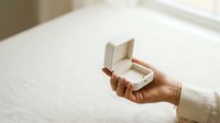 Young woman with medium brown skin tone holding open an elegant white jewelry box displaying a diamond engagement ring, symbolizing marriage proposal and romantic commitment.