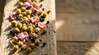 Dried chamomile flowers with rose petals and herbs scattered on rustic wooden surface for natural tea blend and aromatherapy wellness applications.