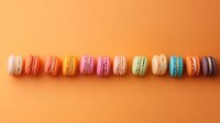 Colorful French macarons arranged in straight line on orange background. Sweet pastel meringue cookies with different flavors and fillings for dessert menu or bakery promotion.