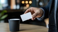 Businessman in formal suit holding blank business card with coffee cup on wooden table in modern office environment.