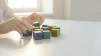 Hands arranging colorful wooden blocks with symbols on white table in bright room for educational play and learning development activities.
