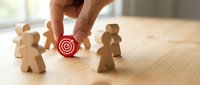 Hand selecting target icon among wooden human figures representing strategic business targeting and customer segmentation for marketing success.