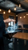 Businessman hand hovering over tablet with glowing digital gears hologram in modern industrial office space with exposed brick walls and pendant lighting.
