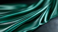 Luxurious emerald green silk fabric with soft folds and waves creates dramatic lighting effect against dark textured surface, suitable for fashion and luxury designs.