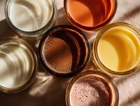 Assortment of colorful beverages in glass cups from top view, including white, orange, brown, clear, and yellow drinks for food photography.