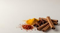 Aromatic spices including cinnamon sticks, star anise, turmeric and paprika powder arranged on neutral background for culinary and cooking projects.