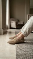 Person wearing beige loafers standing on neutral carpet in modern minimalist hallway with polished floor, natural light, and contemporary furniture visible in background.