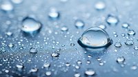 Clear water drops on blue waterproof surface create natural pattern with one large central droplet showing surface tension and light reflection. Macro photography.