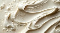 Creamy white frosting texture with smooth swirls and delicate air bubbles creates luxurious bakery background for food photography and dessert marketing.