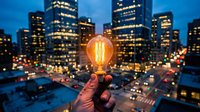Hand holding glowing vintage light bulb against urban cityscape at dusk with illuminated skyscrapers and traffic lights creating bokeh effect for innovation concepts.