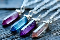 Colorful crystal pendants on silver chains arranged on wooden surface. Healing gemstone jewelry with amethyst, quartz and other natural stones for spiritual wellness.