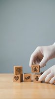 Hands in medical gloves arranging wooden blocks with healthcare symbols including brain, heart, meditation, nature and medical cross on wooden surface.
