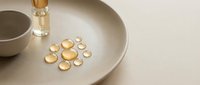 Vitamin D or omega-3 fish oil capsules arranged on a neutral beige plate with a glass of water and bowl, representing daily supplement routine and wellness.
