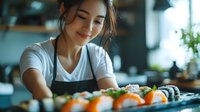 Young Asian woman in apron preparing fresh sushi rolls in modern kitchen setting, focusing on colorful ingredients and traditional Japanese cuisine presentation.