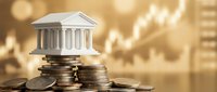Miniature bank building model on stacks of coins with warm golden bokeh background representing financial growth, investment and banking concepts.