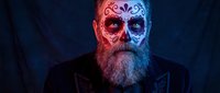 Senior Caucasian man with ornate skull face paint in red and blue colors, dramatic lighting for Halloween costume, Day of the Dead makeup design.