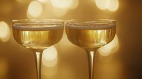 Two champagne coupes filled with sparkling wine against warm golden bokeh lights, perfect for celebration, toast, and festive event photography.