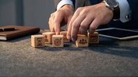Professional businessman arranging wooden blocks with business strategy icons on office desk for corporate planning and goal setting concepts.