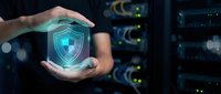 Hands holding glowing shield icon with security lock symbol in server room environment, representing cybersecurity protection and data safety for technology and network defense concepts.