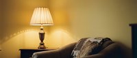 Warm ambient lighting from brass table lamp with pleated shade illuminates cozy living room corner, casting soft glow over upholstered sofa with decorative pillows for interior design and home decor projects.