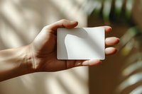 Hand holding blank white credit card mockup with soft natural window shadows perfect for business and banking design presentations.
