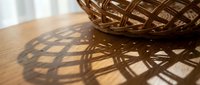 Woven wicker basket casting intricate geometric shadows on wooden surface in warm natural sunlight for home decor and crafts projects.
