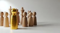 Golden wooden figure standing out from crowd of natural wood pieces representing leadership and uniqueness in business team concept.