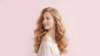 Young woman with long strawberry blonde wavy hair, fair complexion, wearing light pink top against soft pink background. Suitable for beauty, haircare, wellness and lifestyle marketing.