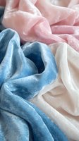 Soft velvet fabric in pastel pink, blue and white colors creating gentle folds and waves, macro shot showing luxurious textile texture and light reflection.