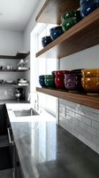 Modern kitchen with floating wooden shelves displaying colorful ceramic bowls and mugs above white subway tile backsplash, marble countertop, and stainless steel sink with window light for home decor and interior design inspiration.