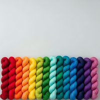 Colorful rainbow yarn skeins arranged in gradient from red to purple on white background for crafting and knitting projects.
