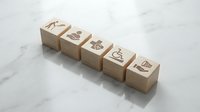 Wooden blocks with engraved icons displaying various symbols including lightbulb, gear, target, and growth chart arranged in row on marble surface.