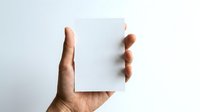 Person holding blank white card or paper against neutral background for mockup, branding, advertising, or presentation purposes.