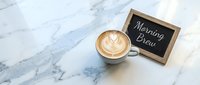 Latte art cappuccino beside a chalkboard sign reading Morning Brew on a white marble surface, top view, cafe and coffee shop concept.