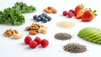Superfood collection with fresh berries nuts seeds and vegetables arranged on white background for healthy eating and nutrition concepts.