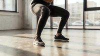 Athletic woman performing squat exercise in modern gym studio with natural lighting for fitness training and strength building workout routine.