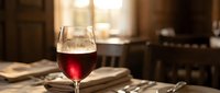 Glass of red wine on wooden table in cozy restaurant setting with warm lighting and blurred background creating intimate dining atmosphere.