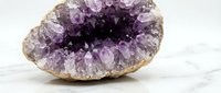 Natural amethyst geode with purple crystals on marble surface for healing, meditation and spiritual wellness practices.