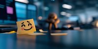 Yellow sticky note with hand drawn smiling face on office desk against blurred workplace background, expressing positive workplace atmosphere and communication.