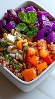 Vibrant buddha bowl with quinoa, purple cabbage, butternut squash, feta cheese, pine nuts and fresh mint garnish served in white ceramic bowl for healthy eating.