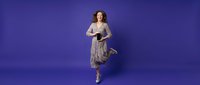 Young woman in flowing gray dress dancing gracefully against vibrant purple studio background. Professional portrait for fashion and lifestyle projects.