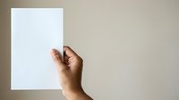 Male hand with medium skin tone holding blank white paper sheet against neutral beige background, suitable for advertising, marketing mockups, presentations, and promotional campaigns.